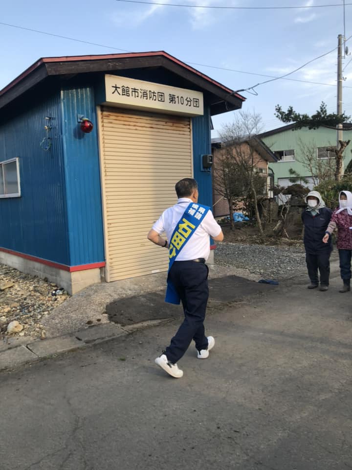 大館市消防団第10分団詰所の前を走り、地元住民と交流する石田ひろしの写真
